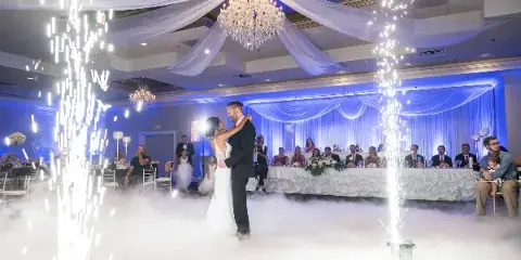 A bride and groom dancing in a large banquet hall with sparkler fountains and low fog effects.