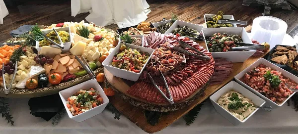 A catering buffet table featuring a large charcuterie board, cheese platter, and assorted side dishes.