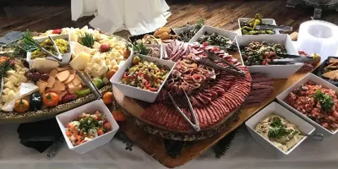A catering buffet table featuring a large charcuterie board, cheese platter, and assorted side dishes.