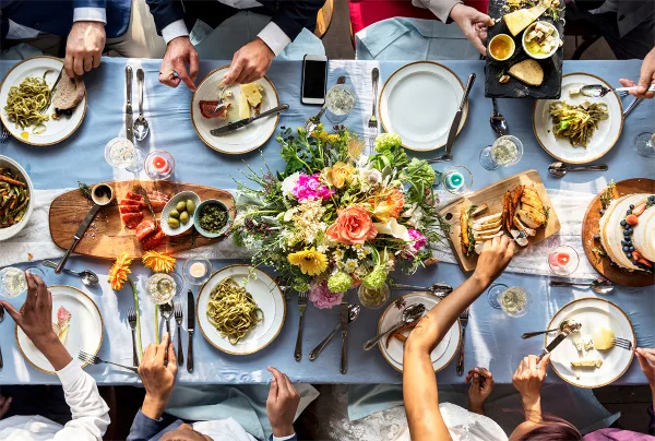Overhead view of a formal dining table set with a floral centerpiece, various plated meals, and guests eating.