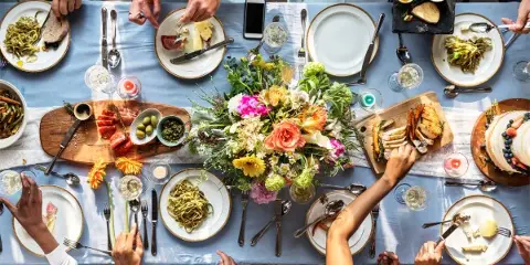 Overhead view of a formal dining table set with a floral centerpiece, various plated meals, and guests eating.