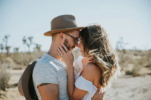 A couple embracing outdoors in a desert landscape with Joshua trees in the background.