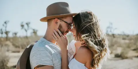 A couple embracing outdoors in a desert landscape with Joshua trees in the background.