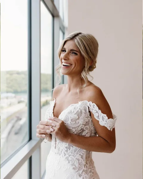 Bride with styled hair and makeup smiling by a window