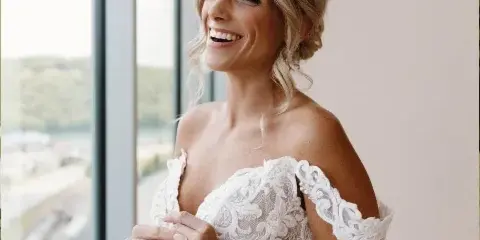 Bride with styled hair and makeup smiling by a window