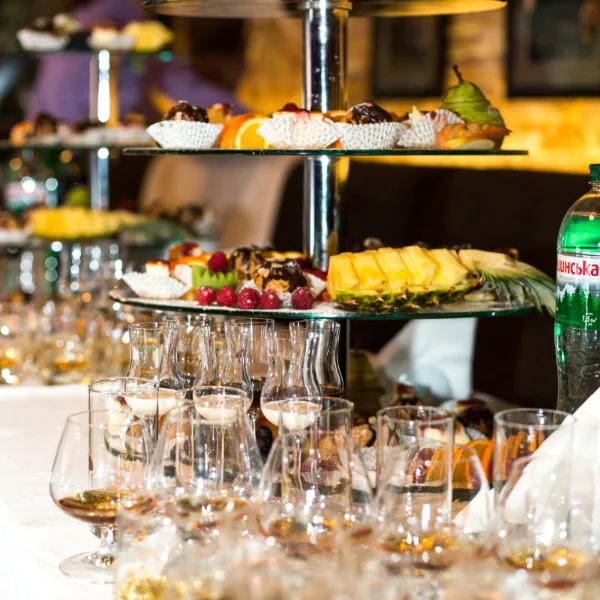 Tiered catering trays filled with fruit and pastries arranged on a table with glassware.