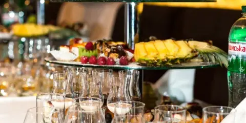Tiered catering trays filled with fruit and pastries arranged on a table with glassware.