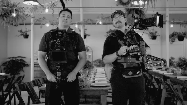 Two videographers holding professional camera equipment in a decorated event venue.