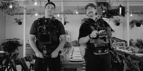 Two videographers holding professional camera equipment in a decorated event venue.