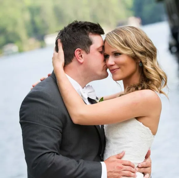 A bride and groom kissing in front of a lake and mountains.
