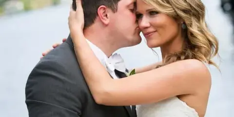 A bride and groom kissing in front of a lake and mountains.