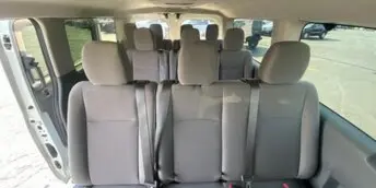 Interior view of a passenger van showing rows of bench seating and headrests.