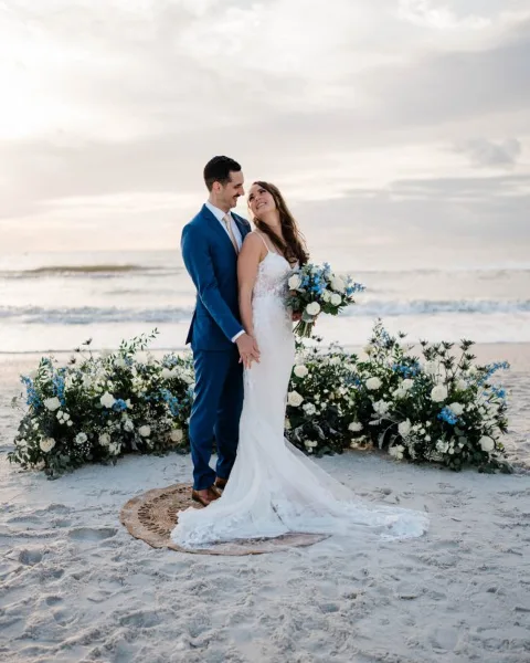 A bride and groom standing on a beach during a wedding ceremony.