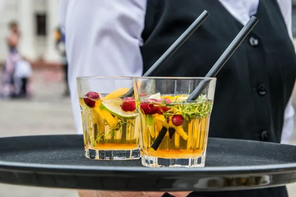 Bartender in a black vest carrying a tray with two garnished cocktails