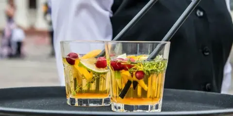 Bartender in a black vest carrying a tray with two garnished cocktails