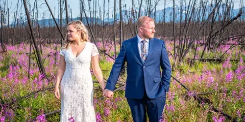 A bride and groom holding hands while walking through a field of purple wildflowers.
