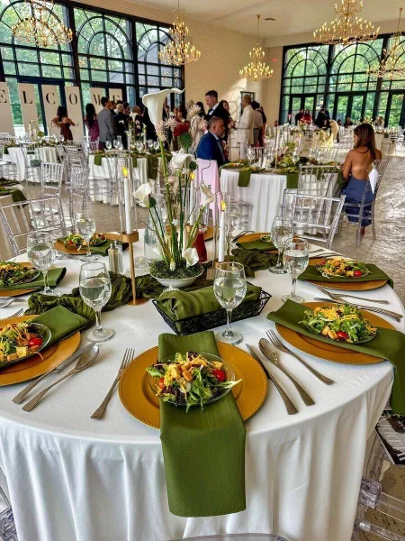 Wedding reception table styled with green napkins, gold chargers, calla lily centerpiece, and WELCOME signage in the background.