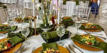 Wedding reception table styled with green napkins, gold chargers, calla lily centerpiece, and WELCOME signage in the background.