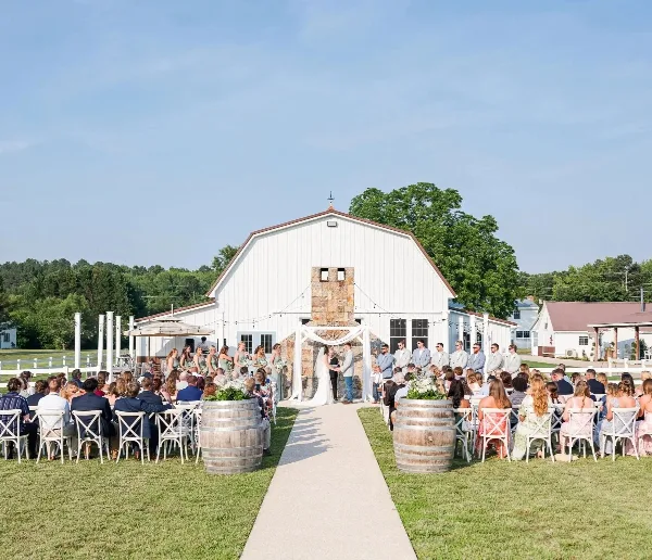 An outdoor wedding ceremony with a bride and groom at an altar in front of a white barn venue.