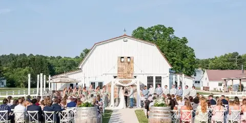 An outdoor wedding ceremony with a bride and groom at an altar in front of a white barn venue.