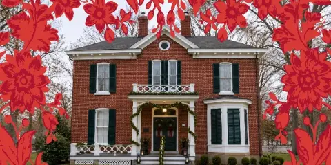 Exterior view of a two-story red brick historic house with white trim and green shutters, decorated with holiday garlands.