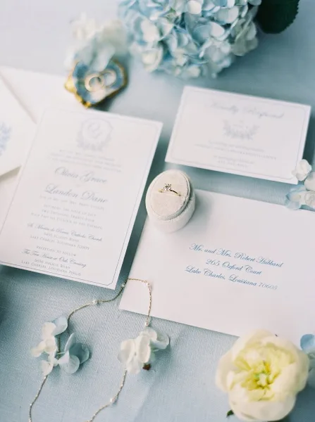 A flat lay photograph of a wedding invitation suite, rings, and floral details.