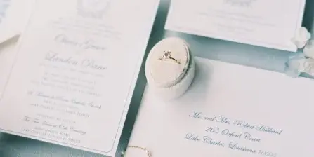 A flat lay photograph of a wedding invitation suite, rings, and floral details.