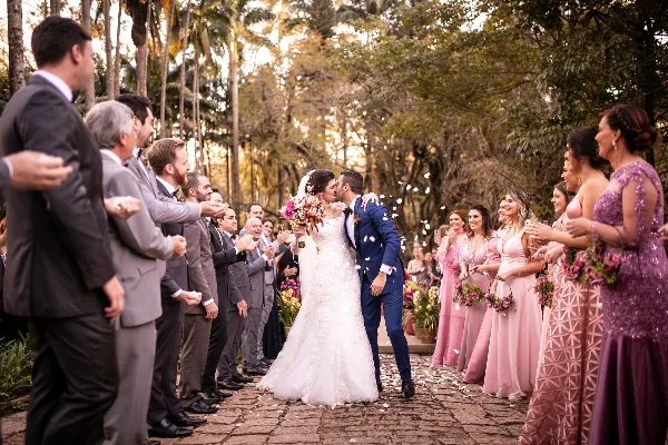 A bride and groom kissing during a wedding ceremony while guests line the aisle and throw petals.