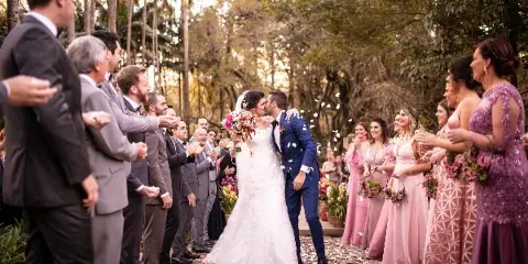 A bride and groom kissing during a wedding ceremony while guests line the aisle and throw petals.