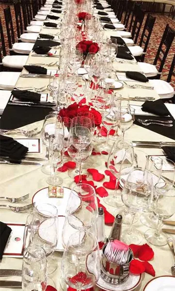 A long banquet table set with white linens, black napkins, red rose centerpieces, and glassware.