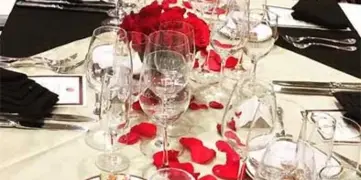 A long banquet table set with white linens, black napkins, red rose centerpieces, and glassware.