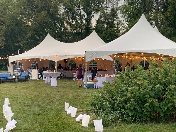 White event tent set up on a lawn with tables, chairs, and string lights for a wedding or party.
