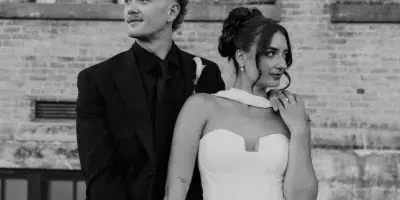 Black and white portrait of a bride and groom standing together in front of a brick wall.