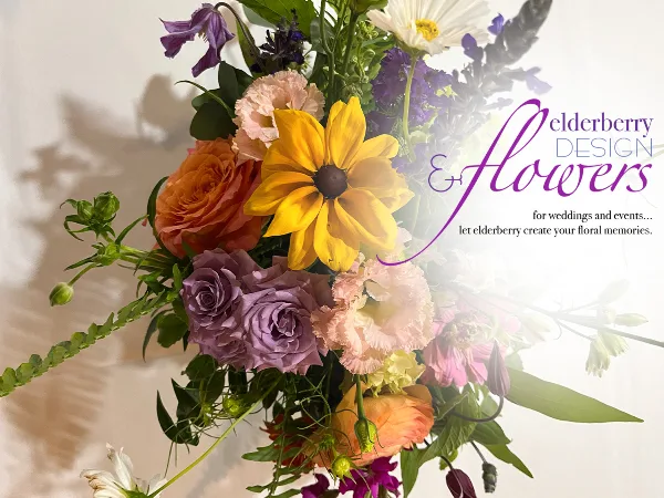 A vibrant floral arrangement featuring yellow daisies, orange and purple roses, and greenery.