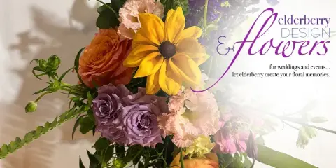 A vibrant floral arrangement featuring yellow daisies, orange and purple roses, and greenery.
