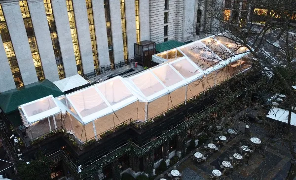 Aerial view of a large, illuminated clear-top frame tent installed on a city rooftop.