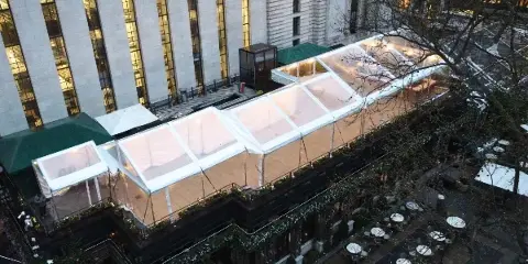 Aerial view of a large, illuminated clear-top frame tent installed on a city rooftop.