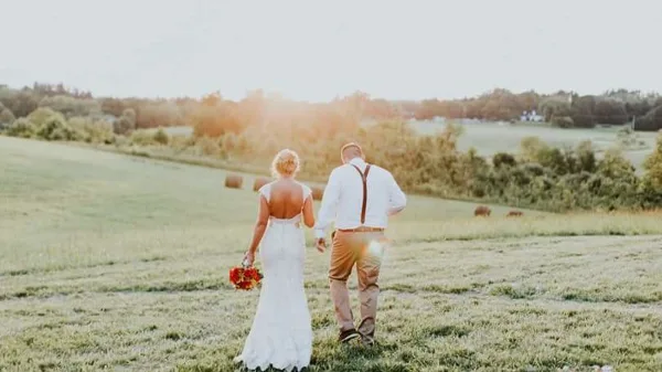 A bride and groom walking away from the camera in a grassy field at sunset.