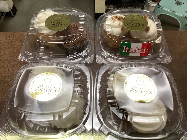 Four plastic containers of baked goods, including cupcakes and cheesecakes, each labeled with a Sally's Piece-a-Cake sticker.