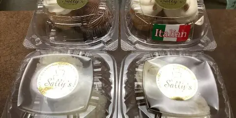 Four plastic containers of baked goods, including cupcakes and cheesecakes, each labeled with a Sally's Piece-a-Cake sticker.