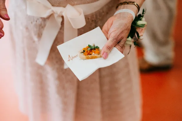 A person in a formal dress holds a small appetizer on a branded white napkin.