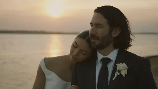 Cinematic still of a bride and groom embracing at sunset by the water