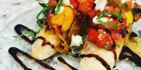 A close-up of a plated appetizer featuring bread topped with tomatoes, cheese, and basil, garnished with a balsamic drizzle.