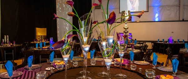 A decorated event table with blue napkins, glassware, and tall floral centerpieces in a banquet hall.