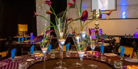 A decorated event table with blue napkins, glassware, and tall floral centerpieces in a banquet hall.