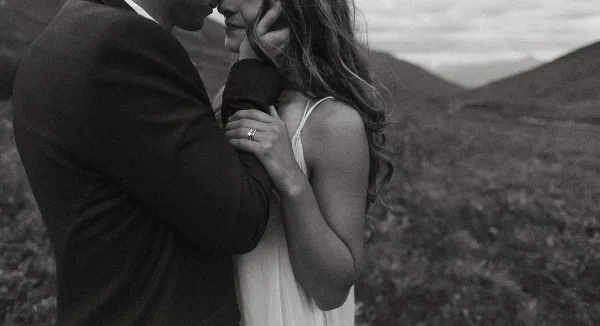 Black and white photo of a couple embracing outdoors with a wedding ring visible