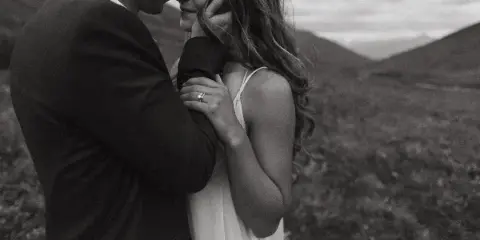Black and white photo of a couple embracing outdoors with a wedding ring visible