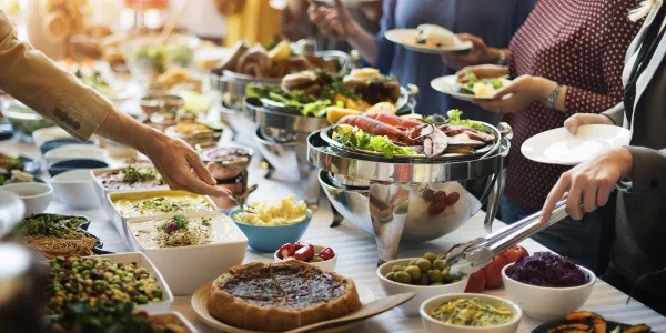A catering buffet table with chafing dishes, salads, and guests serving themselves plates of food.