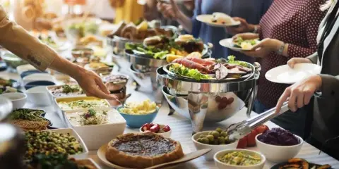 A catering buffet table with chafing dishes, salads, and guests serving themselves plates of food.