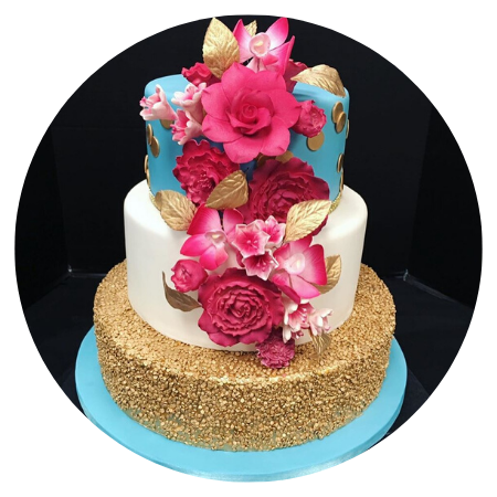 A three-tiered custom cake featuring a gold-dusted base, a white middle tier, and a blue top tier, decorated with vibrant pink and red fondant roses and gold leaves.